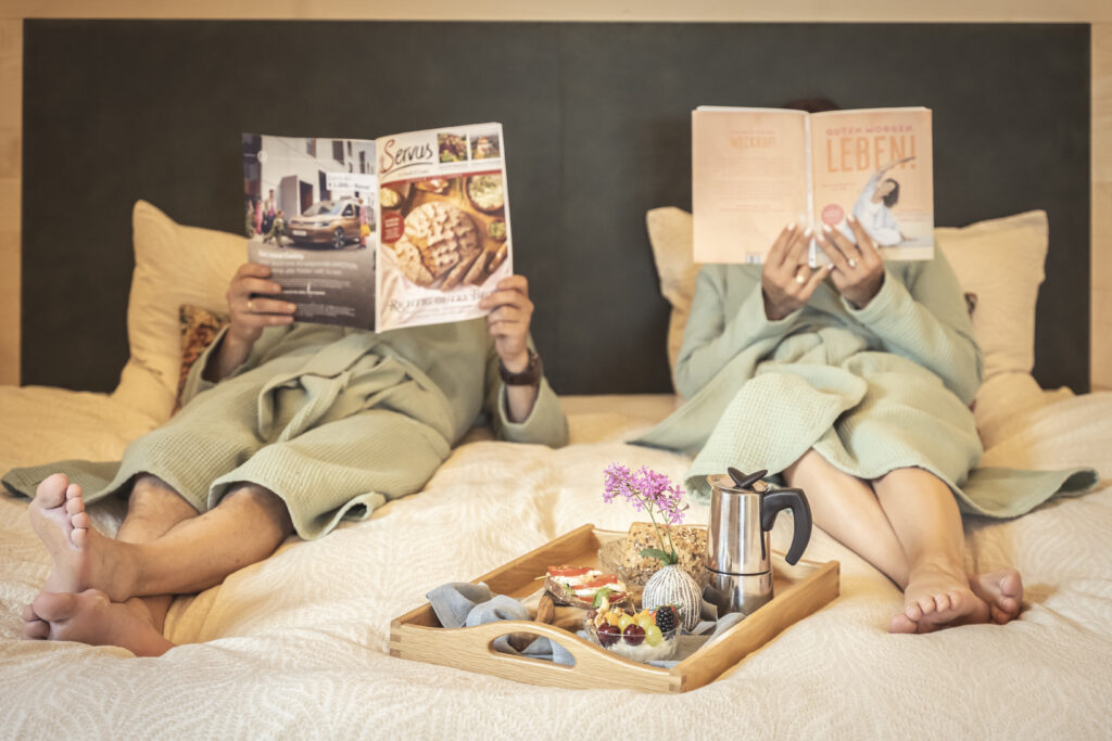 Zwei Gäste im Bademantel die eine Zeitschrift im Bett lesen