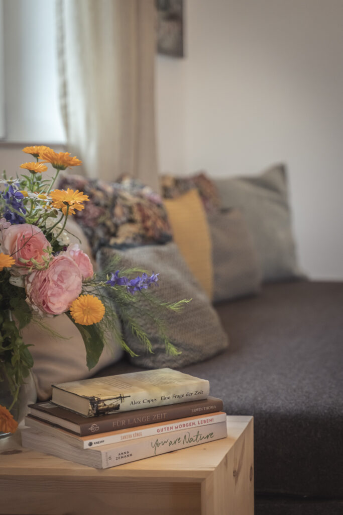 Blumenstrauß und Bücherstapel auf dem Holztisch vor dem Sofa der Suite Federweiß