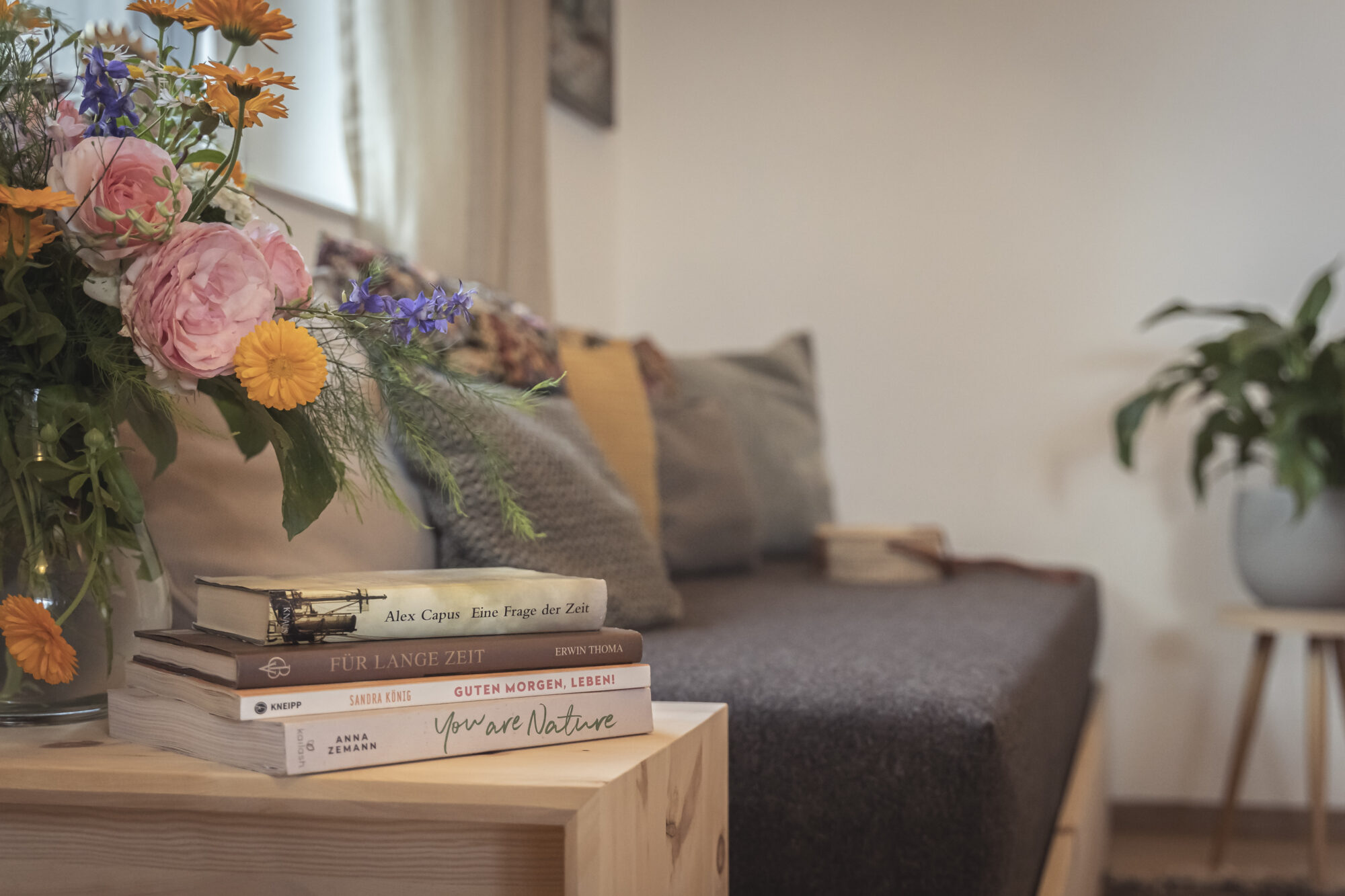Blumen und Bücher auf dem Holztisch vor dem Sofa der Suite Federweiß, dahinter das Fenster